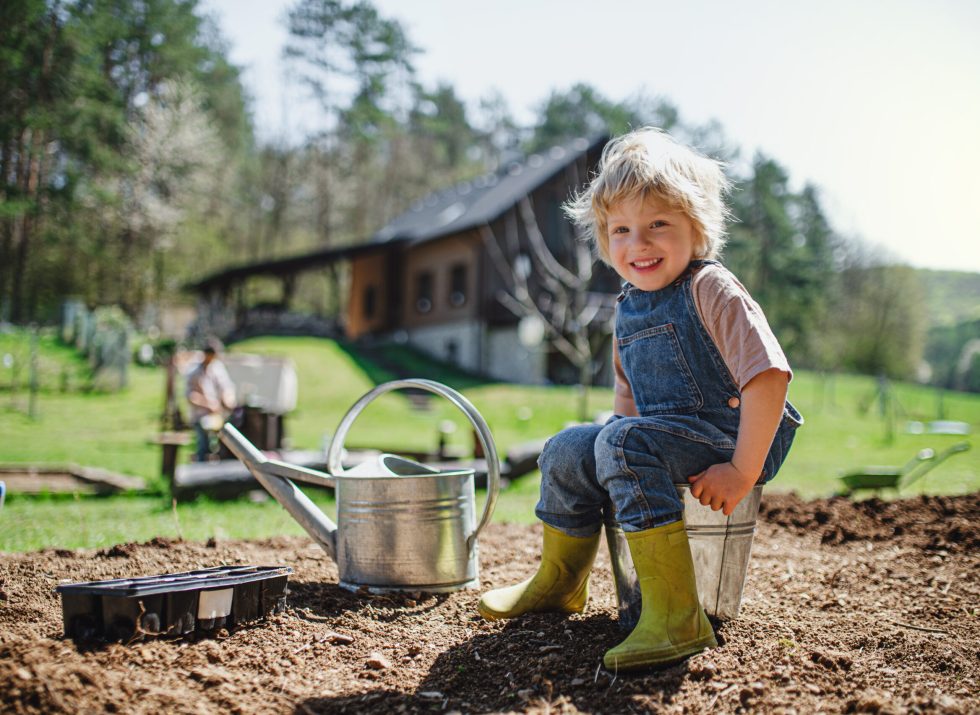 Happy small boy working outdoors in garden, sustainable lifestyle concept.